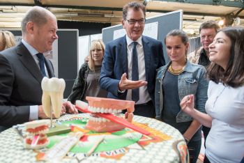 Das Bild zeigt den Ersten Bürgermeister Olaf Scholz und Bundesentwicklungsminister Dr. Gerd Müller mit Schülerinnen, die Zahnprophylaxe anhand von großen Plastikgebiss und Zahnbürste erklären.